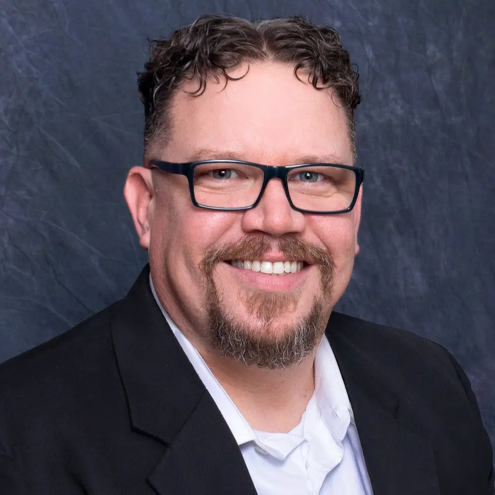 Photo of a smiling man with a goatee and glasses in a dress shirt and blazer