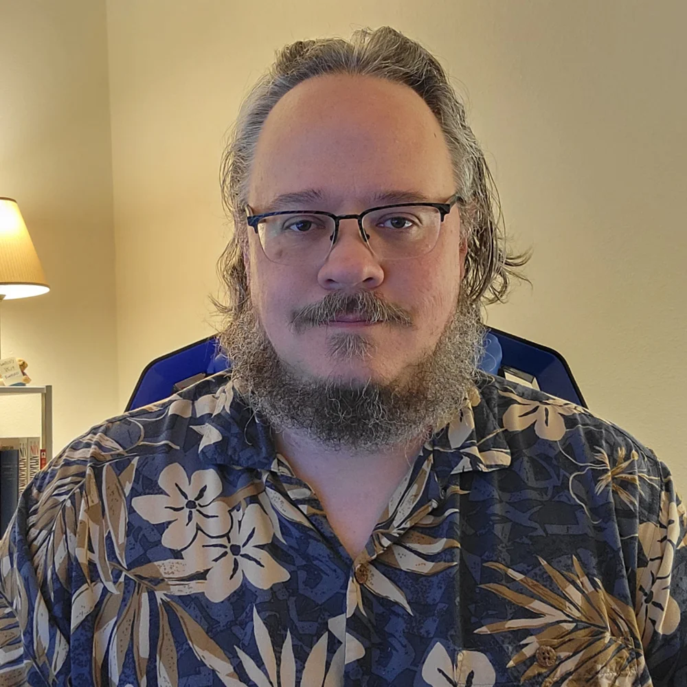Photo of a smiling man with a beard and glasses in a sport shirt